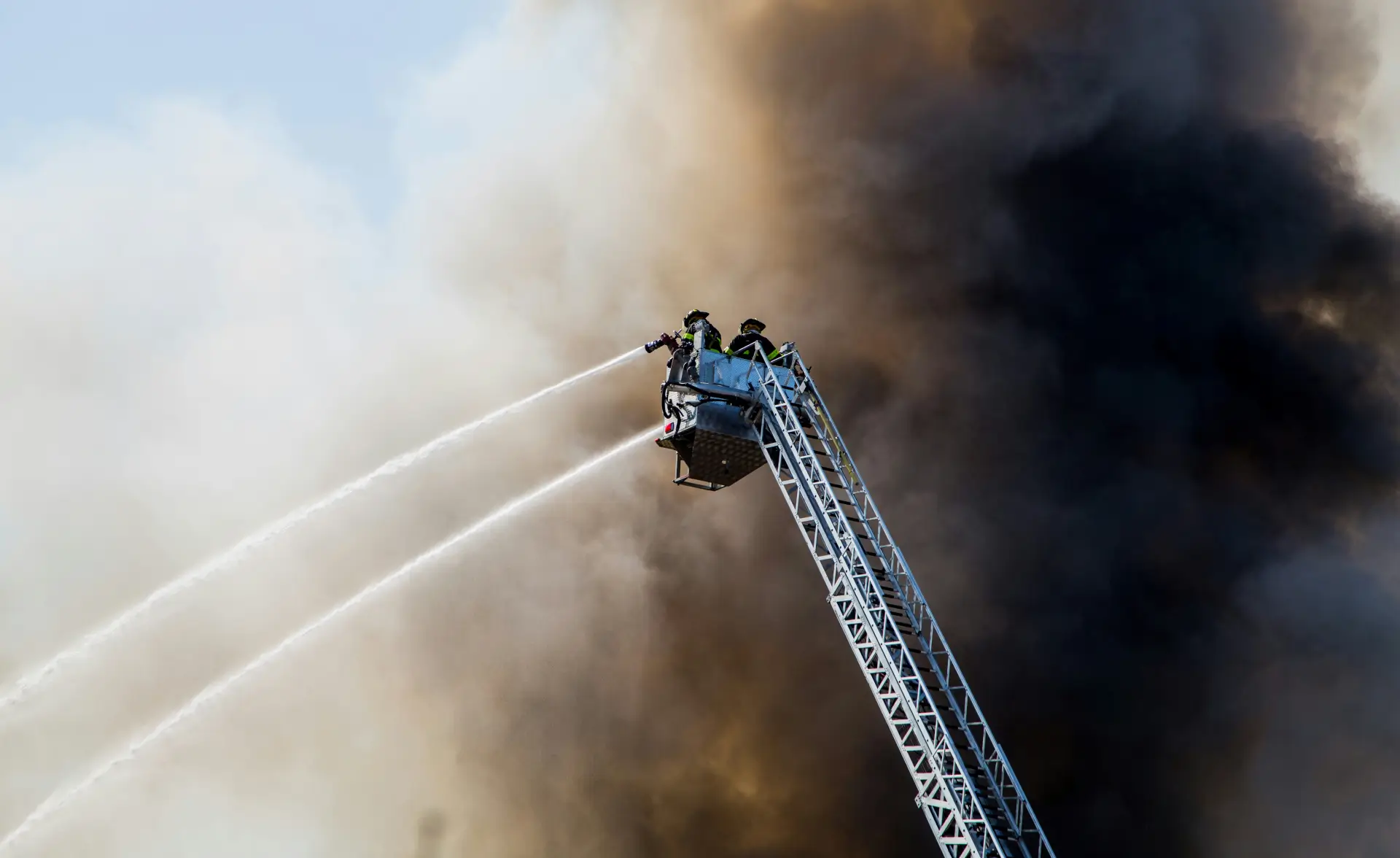 Firefighters on a ladder spraying water into thick smoke