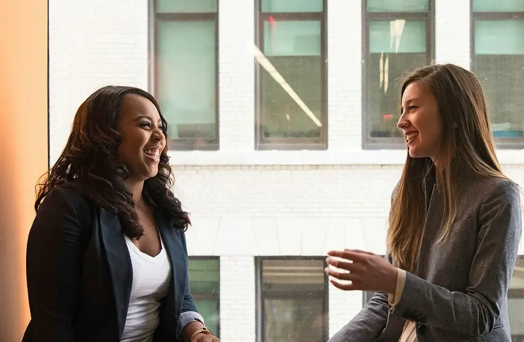 Two colleagues talking and laughing beside an office window