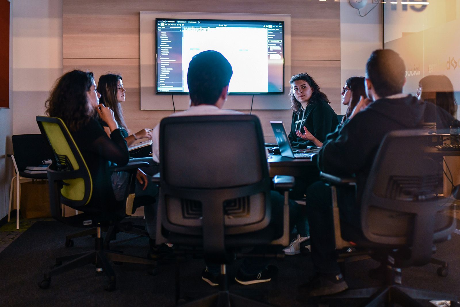 Team seated around a conference table watching a presentation on a wall screen
